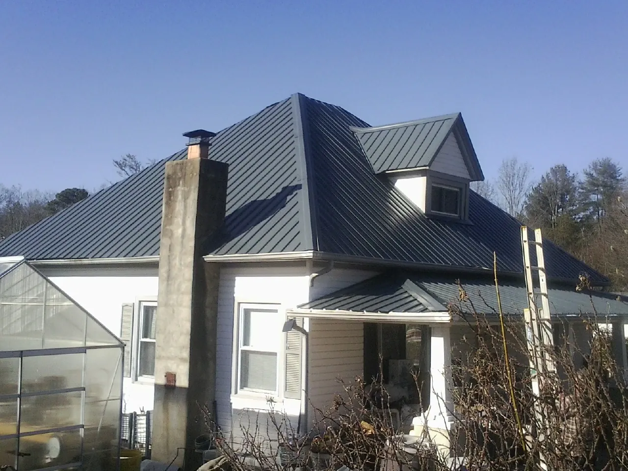 Dark blue standing seam metal roof on a white farmhouse with dormer — Slate & Tile Roof Repair by Roofing Brothers in Montevallo