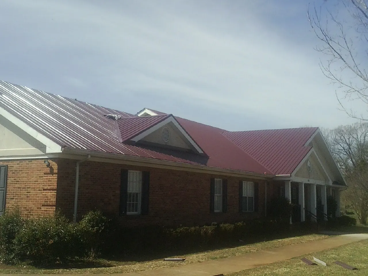 Red metal roof with gabled entries on a long brick building, from a Hail Damage Roof Repair job in Montevallo