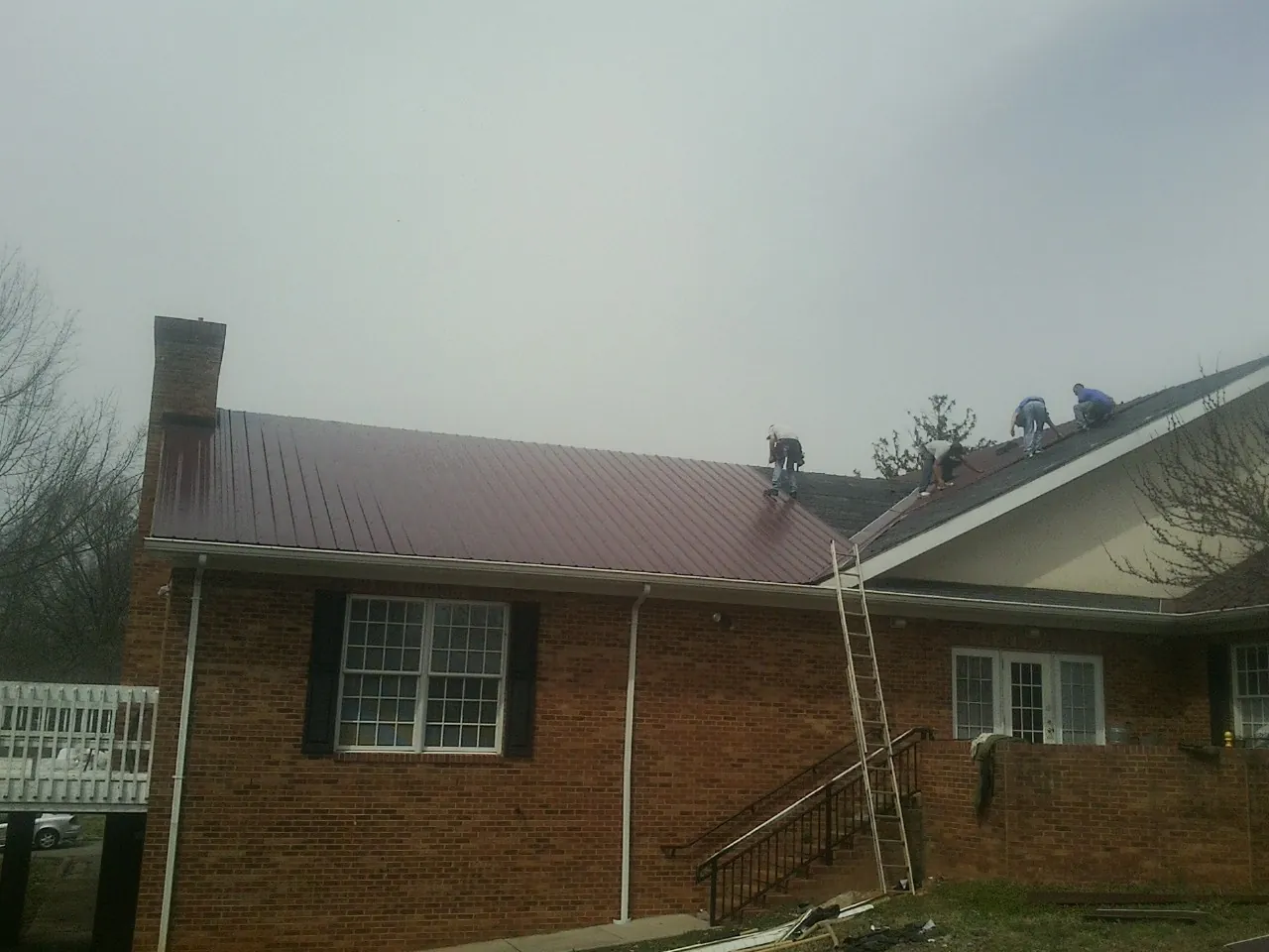Crew setting red metal roofing panels on a brick home in Montevallo