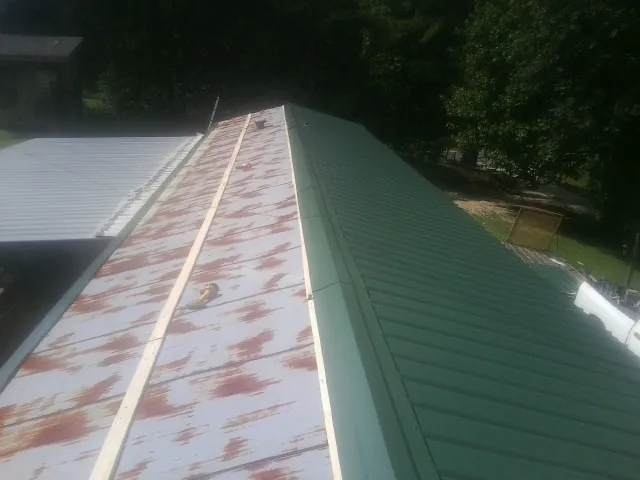 Old rusted panels beside newly installed green metal roofing — Wind Damage Roof Repair by Roofing Brothers in Montevallo