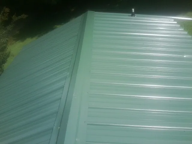 New green metal panels meeting at the ridge of a roof — Flat Roof Repair work by our crew in Montevallo