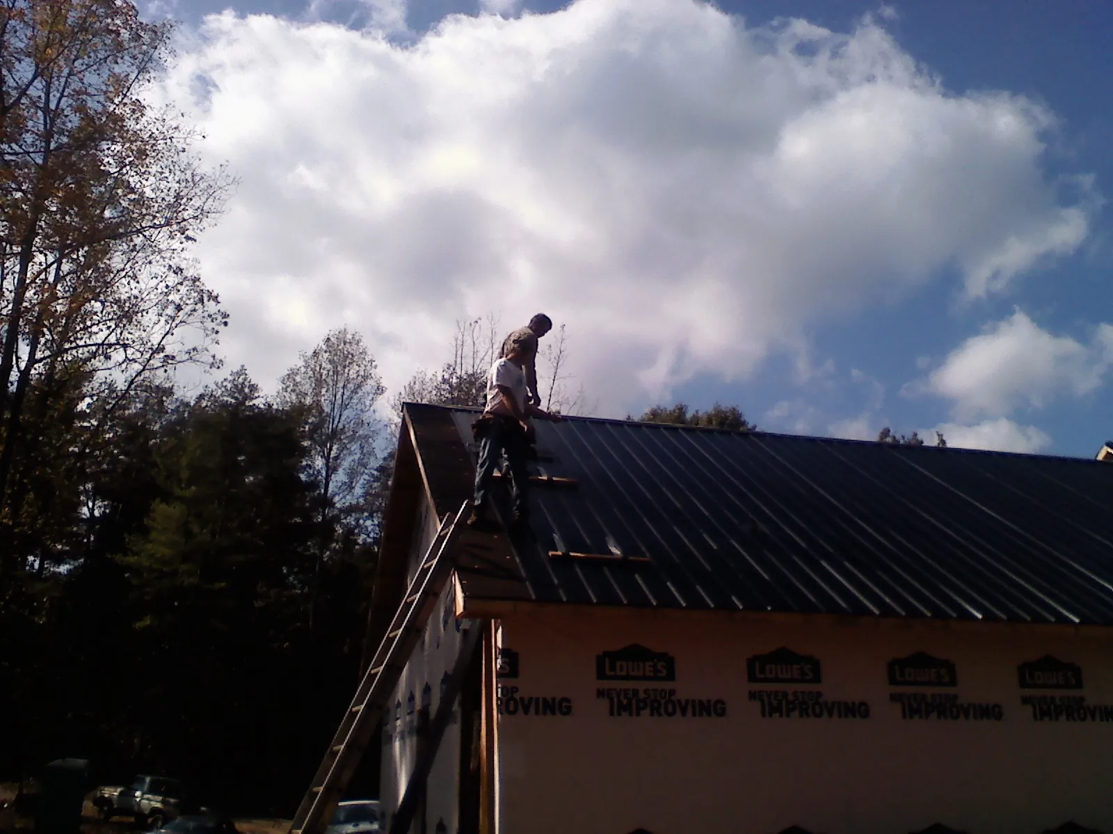 Roofer fastening dark metal panels high against a cloudy sky, from a Roof Inspection job in Montevallo