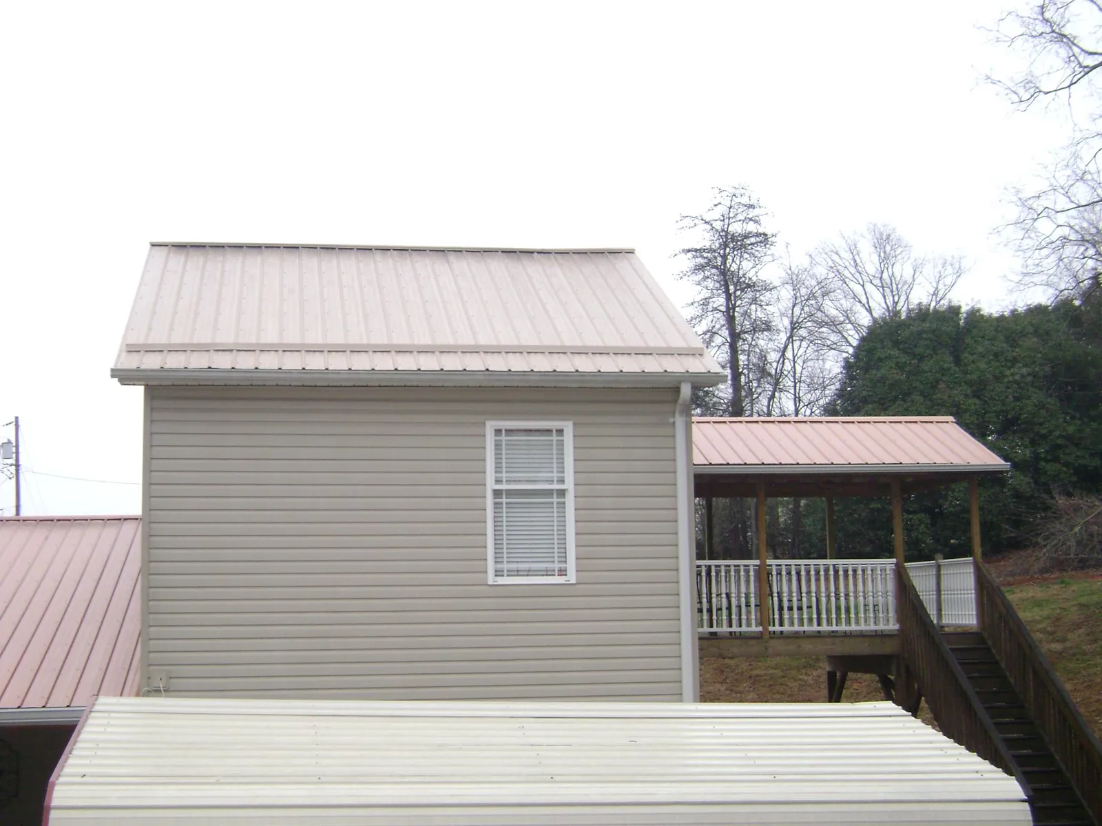 Tan metal roofs on a two story addition and attached porch, from a Roof Replacement job in Montevallo